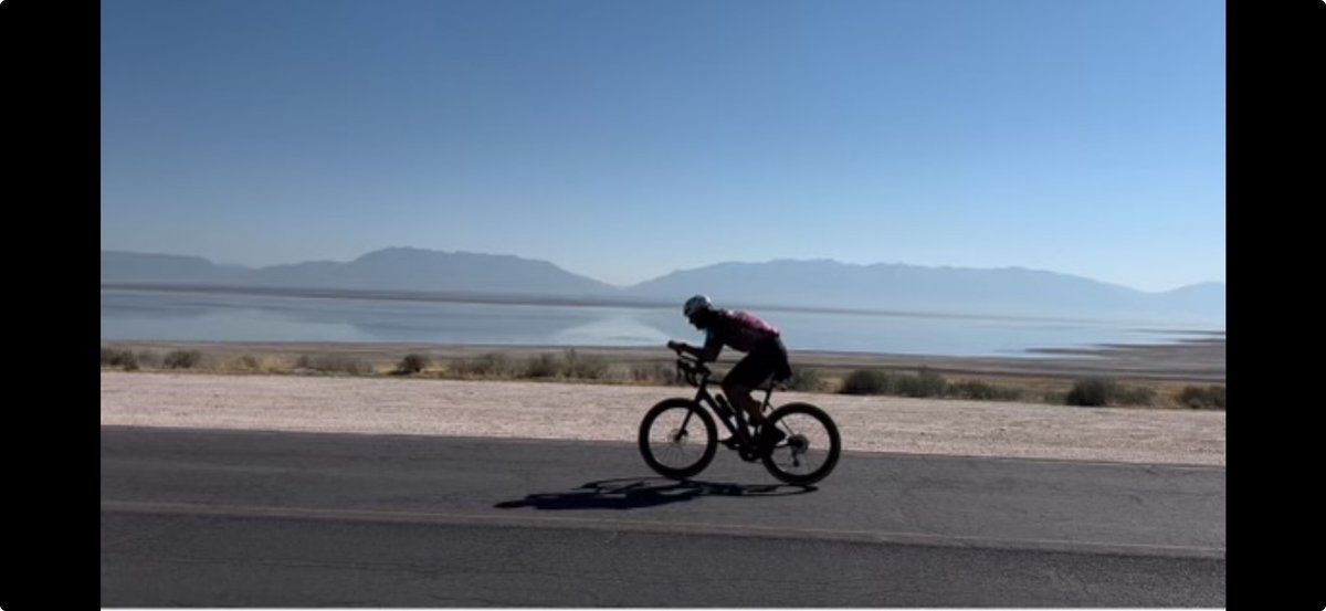 Justin Manco riding a road bike along the Great Salt Lake during a triathlon, mountains in the background.